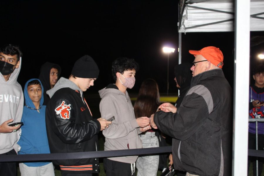 Junior Alex Ahmed shows his student identification at the entrance, in order to get in to the home football game on Oct. 22, 2021. My friend was able to get in even though he didnt have his ID, because Mr. Maher, whos standing at the entrance, knows him, Ahmed said. The football team lost to Plymouth Canton by a final score of 44 to 43.